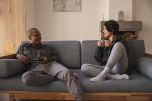 Couple sitting on a gray couch and having a casual conversation over coffee.